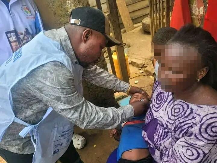 Agent de santé en gilet bleu PEV vaccinant un enfant tenu par sa mère lors d'une campagne de santé en zone rurale.